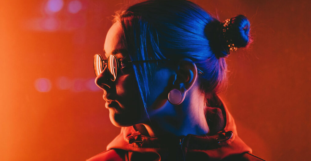 Millennial pretty girl with unusual hairstyle near glowing red neon of city at night. Dyed blue hair in braids. Mysterious hipster teenager in glasses. Reflection of light. Millennial pretty girl with unusual hairstyle near glowing red neon of city at night. Dyed blue hair in braids. Mysterious hipster teenager in glasses. Reflection of light.